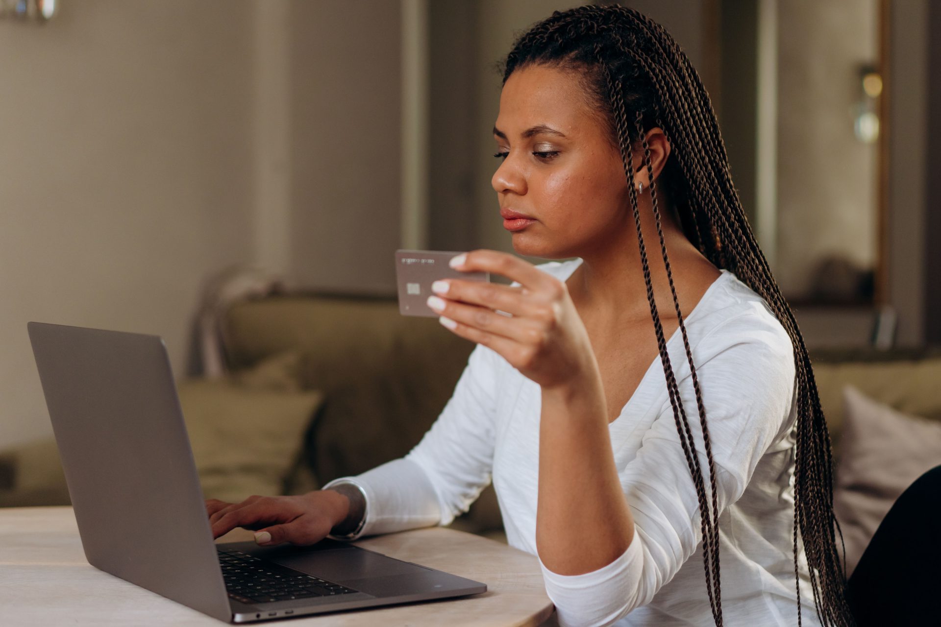 A woman with braided hair makes an online transaction using a credit card and laptop at home.